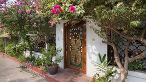 A house with a decorative wooden door, a small garden with potted plants, and a tree with pink flowers. - Exclusive Villa, 6 Bedrooms, Private Pool, Garden View, 10 Mins LK Metro (Pattaya)