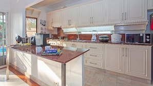 A modern kitchen with white cabinetry, a granite countertop, and various appliances including a coffee maker and microwave. - Exclusive Villa, 6 Bedrooms, Private Pool, Garden View, 10 Mins LK Metro (Pattaya)