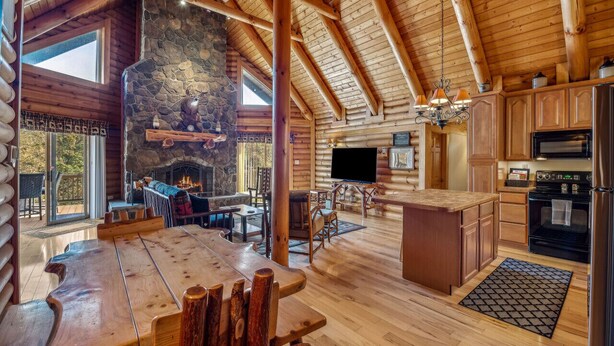 A spacious log cabin interior with a stone fireplace, wooden dining area, and a kitchen with modern appliances. - Overlook at Sleepy Creek -secluded, creek access, grill, wifi, deck, game room (Berkeley Springs)
