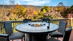 A round outdoor table with four chairs, a fire pit in the center, and two wine glasses. - Overlook at Sleepy Creek -secluded, creek access, grill, wifi, deck, game room (Berkeley Springs)