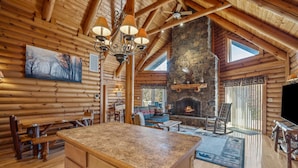 A log cabin interior with a stone fireplace, wooden furniture, and a large window. - Overlook at Sleepy Creek -secluded, creek access, grill, wifi, deck, game room (Berkeley Springs)