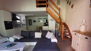 A living room with a dark-colored sectional sofa, a white coffee table, and a white cabinet. A wooden staircase leads to an upper level. - 10 MNS from PORTO VECCHIO MINI VILLA WITH SEASIDE LAND MER-6 People (Saint Lucie de Porto Vecchio)