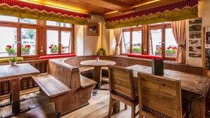 A cozy restaurant with wooden furniture, large windows with curtains, and a warm wooden ceiling. - Hotel De La Poste (Bagnes)