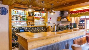 A bar area with a wooden counter, shelves with bottles and glasses, and a clock on the wall. - Hotel De La Poste (Bagnes)