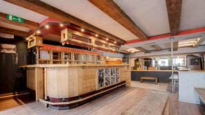 A spacious lobby with a central wooden reception desk, a bench, and a modern kitchen area in the background. - Hotel De La Poste (Bagnes)