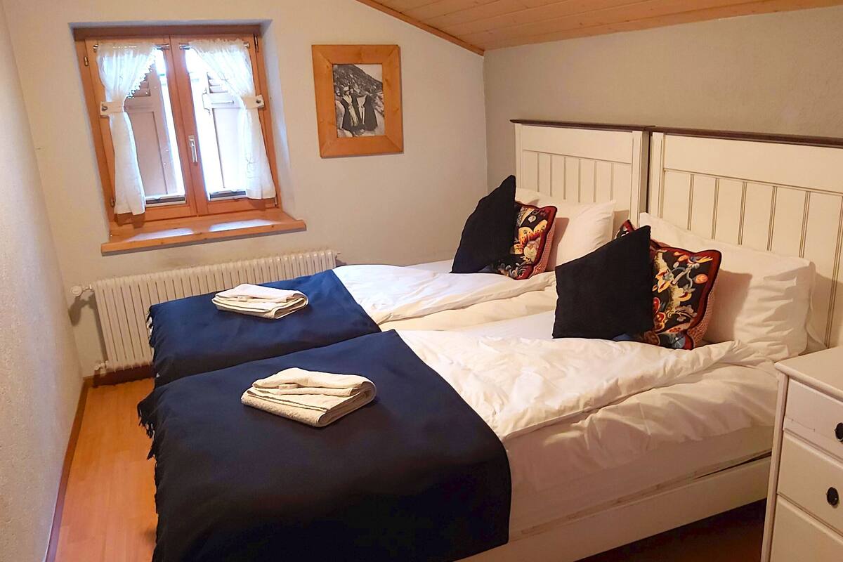 A bedroom with two beds, a window with curtains, a radiator, and a framed picture on the wall.
