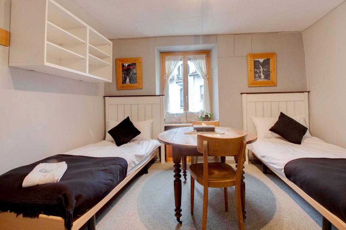 A small room with two single beds, a round table, and a chair.