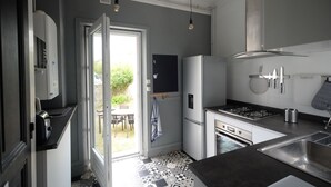 Cozinha compacta com geladeira, fogão e pia. Uma porta dá acesso a uma área externa com mesa e cadeiras.