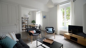 Uma sala de estar moderna com sofá, poltronas, mesa de centro, televisão e área de jantar com mesa e cadeiras.
