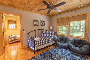 A cozy bedroom with a bed, a gray bean bag chair, a patterned rug, and a window with a view of trees.
