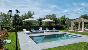 Une piscine entourée de chaises longues et de parasols, elle-même bordée d’une pelouse bien entretenue et d’un kiosque.