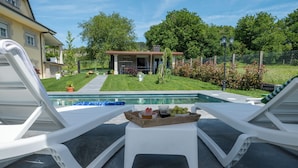 Un espace aménagé au bord de la piscine, avec deux chaises longues blanches et une petite table sur laquelle sont disposés des fruits et une boisson.