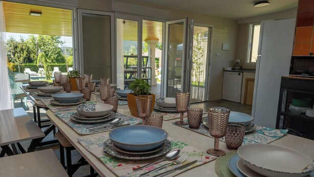 Un espace repas avec une longue table dressée pour accueillir plusieurs personnes, agrémentée de différents types d’assiettes, de bols et de couverts.