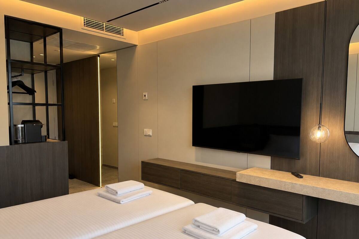 A modern hotel room with a large bed, a flat-screen TV mounted on the wall, a built-in coffee machine, and a walk-in closet.