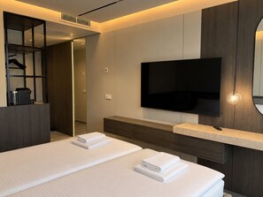 Una habitación de hotel moderna con una cama grande, un televisor de pantalla plana en la pared, una cafetera integrada y un vestidor.
