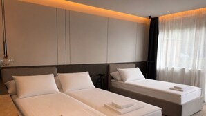 Une chambre d’hôtel moderne avec deux lits, une grande fenêtre avec des rideaux légers et un design minimaliste.
