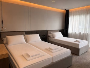 Una habitación de hotel moderna con dos camas, un ventanal con cortinas translúcidas y un diseño minimalista.