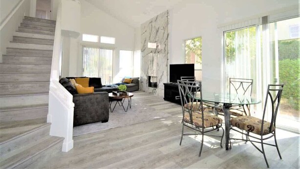 A spacious living area with a staircase, a sofa set, a glass dining table, and a fireplace. - Desert Princess Townhouse Retreat (Cathedral City)