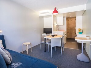 A modern, compact living space with a sofa, a dining table, and a kitchenette.