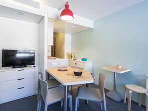 A compact living space with a kitchenette, a dining area with a table and chairs, a television on a stand, and a red pendant light.