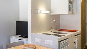 A compact kitchenette with a built-in stove, a sink, and a microwave. There is a television on a small table and a bowl on the countertop.