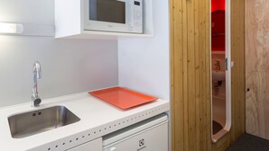 A modern kitchen with a white countertop, stainless steel sink, and a microwave. There's a red tray on the counter and a wooden door with a red interior.