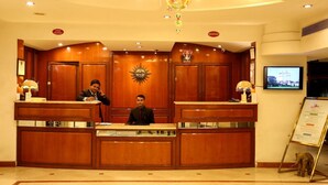 A reception desk with two staff members, a wall-mounted television, and a framed welcome sign. - HOTEL ANS INTERNATIONAL (Raigarh)