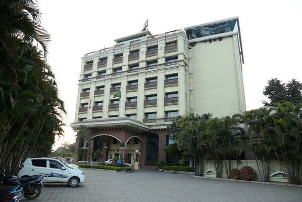 A multi-story hotel with a central entrance, surrounded by palm trees and a paved driveway.