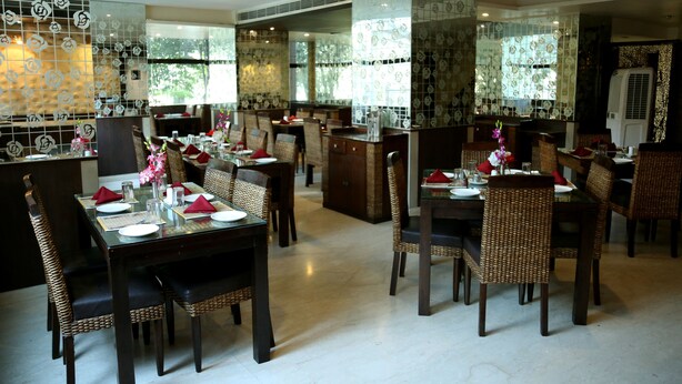 A restaurant with multiple dining tables and chairs, large windows, and decorative wall tiles. - HOTEL ANS INTERNATIONAL (Raigarh)