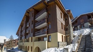 Un hotel de varios pisos con balcones, un telesilla y paisajes nevados.