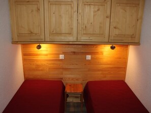 Ein kleines Zimmer mit zwei Betten, Holzschränken darüber und Holzboden.