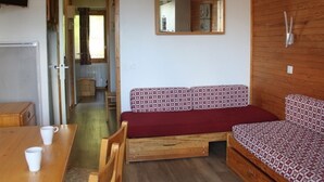 Habitación pequeña con un sofá de madera, una mesita con dos tazas blancas, un espejo en la pared y un mueble de madera.