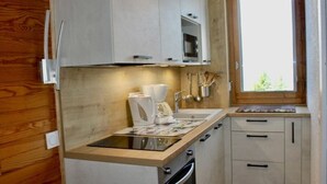 Cocina compacta con gabinetes de madera, horno empotrado, cafetera y ventana con vistas a zonas verdes.