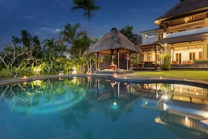 A swimming pool with a thatched-roof gazebo, surrounded by lush greenery and a large house with a balcony. - Villa Djani Balangan by Nagisa Bali (Ungasan)