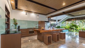 A modern kitchen with a central island, built-in appliances, and a view of lush greenery outside. - Villa Djani Balangan by Nagisa Bali (Ungasan)