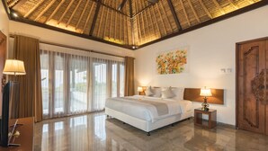 A spacious bedroom with a large bed, a ceiling fan, a painting, and a wooden door. - Villa Djani Balangan by Nagisa Bali (Ungasan)