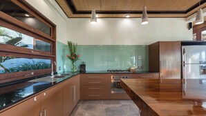 A modern kitchen with wooden cabinets, a large island, and a view of the outdoors. - Villa Djani Balangan by Nagisa Bali (Ungasan)