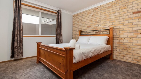 A single bed in a room with a brick wall and a window with curtains.
