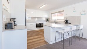 A modern kitchen with white cabinetry, a central island with bar stools, a built-in oven, and a coffee maker.