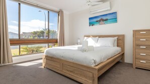 A bedroom with a wooden bed, a nightstand, a dresser, and a large window offering a view of the outdoors.