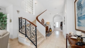 A spacious living area with a curved staircase, a large window, and a view of the living room. - OceanView,3500sqft,60sec Beach Access! 4 bedrooms with 4 ensuite baths&Elevator! (South Padre Island)