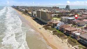 A coastal hotel with a beach view, multiple floors, and a prominent building in the background. - OceanView,3500sqft,60sec Beach Access! 4 bedrooms with 4 ensuite baths&Elevator! (South Padre Island)