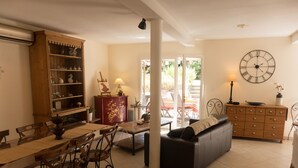 A living room with a dining area, a sofa, a wooden cabinet, and a wall clock. - Air conditionned house in a quiet village private pool in large closed garden  (Azille)