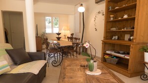 A living room with a wooden coffee table, a sofa, a dining table with chairs, and a bookshelf. - Air conditionned house in a quiet village private pool in large closed garden  (Azille)