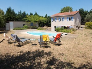 A backyard with a swimming pool, three lounge chairs, and a house with a red-tiled roof.