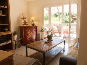 Ein Wohnzimmer mit Couchtisch aus Holz, einem roten Schrank mit floralen Schnitzereien, einer Lampe und Blick auf eine Terrassenanlage mit Stühlen und Tisch.