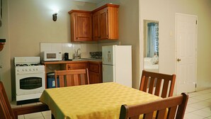 A compact kitchen with wooden cabinets, a microwave, a stove, and a refrigerator. - King Suite with Kitchenette at Bellissimo (Buccoo)