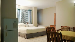 A small, clean room with two beds, a table, and a chair. - King Suite with Kitchenette at Bellissimo (Buccoo)