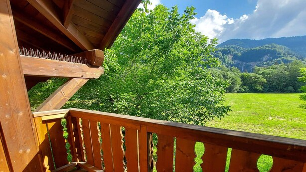 Un balcon en bois offrant une vue sur un paysage verdoyant et luxuriant, avec des montagnes en arrière-plan.