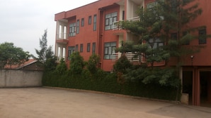 A red building with multiple windows and balconies, surrounded by greenery. - DAKS HOTEL KIRINYA (Kampala)